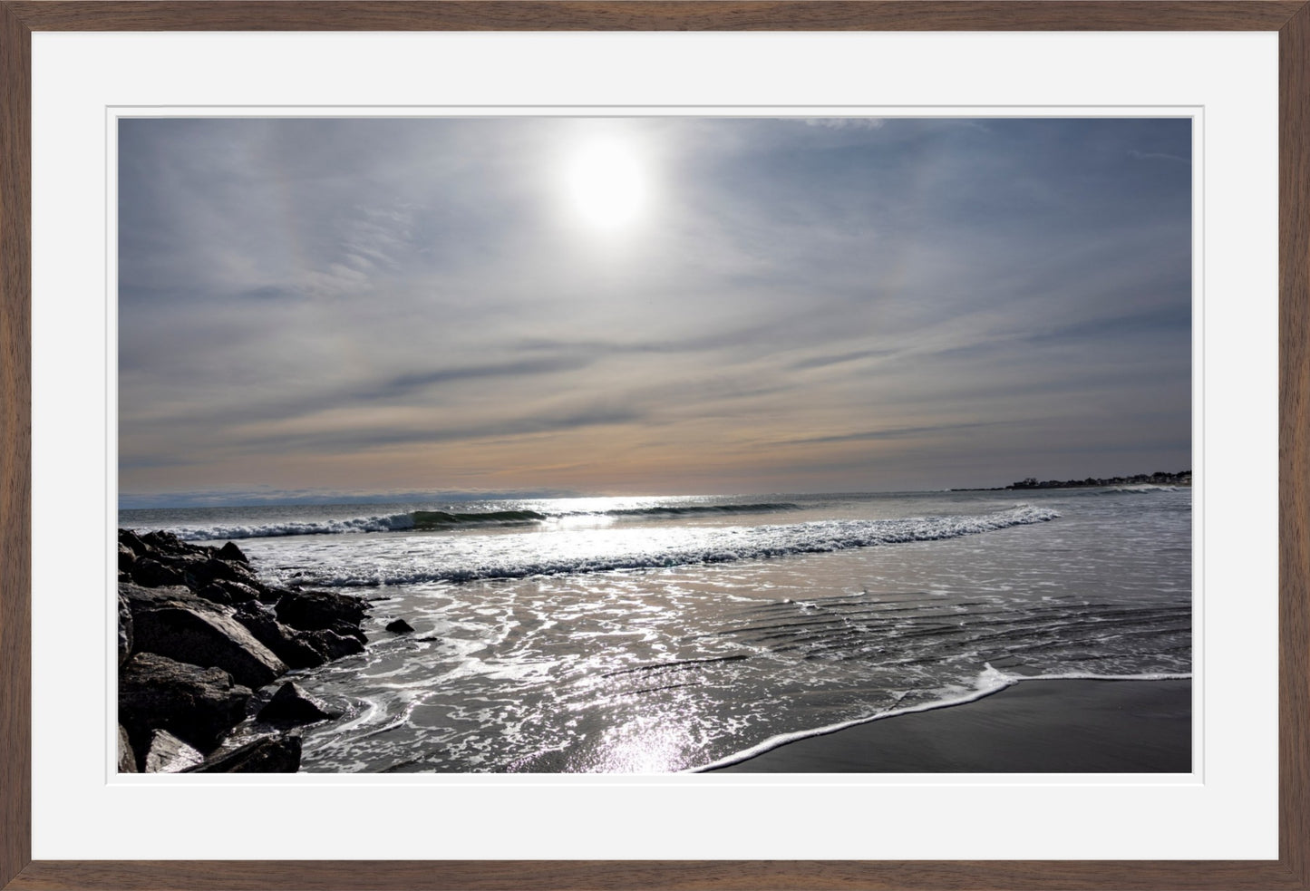 Beach scene with waves and rocks under a sunlit sky, framed with a border
