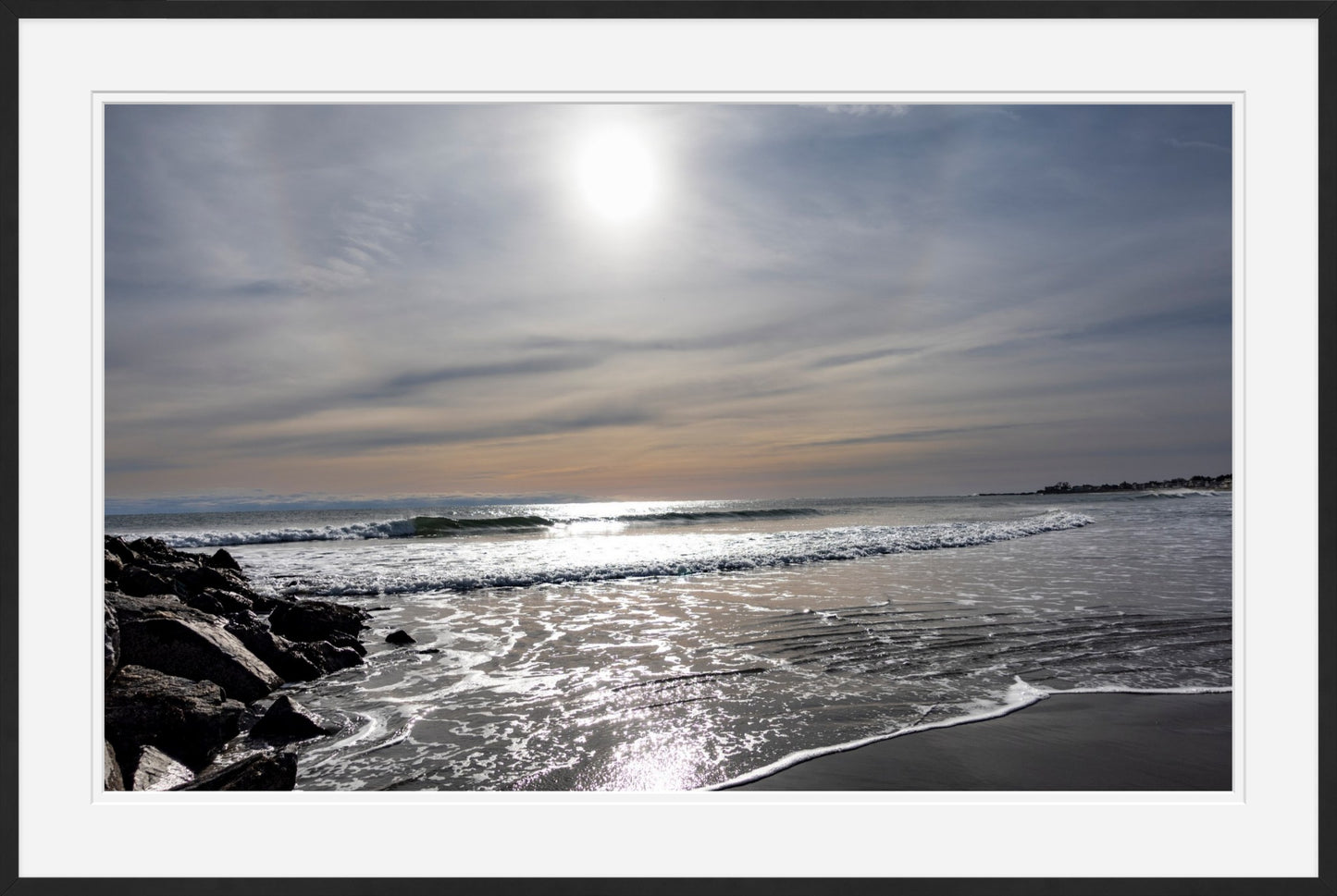 Sunset over a beach with waves and rocks and a slim black frame