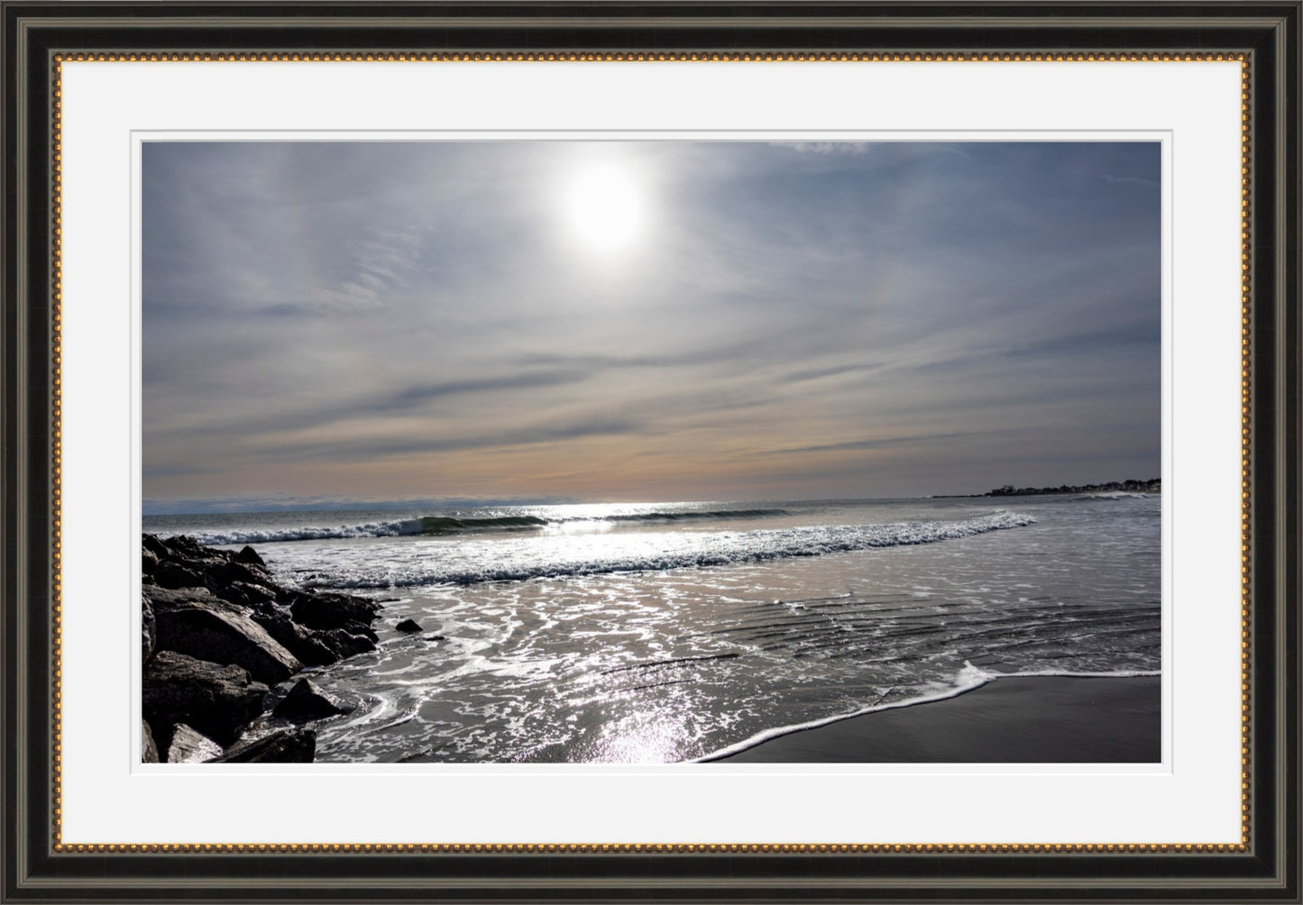 Framed photograph of a beach scene with waves and rocks, framed with a gold border.