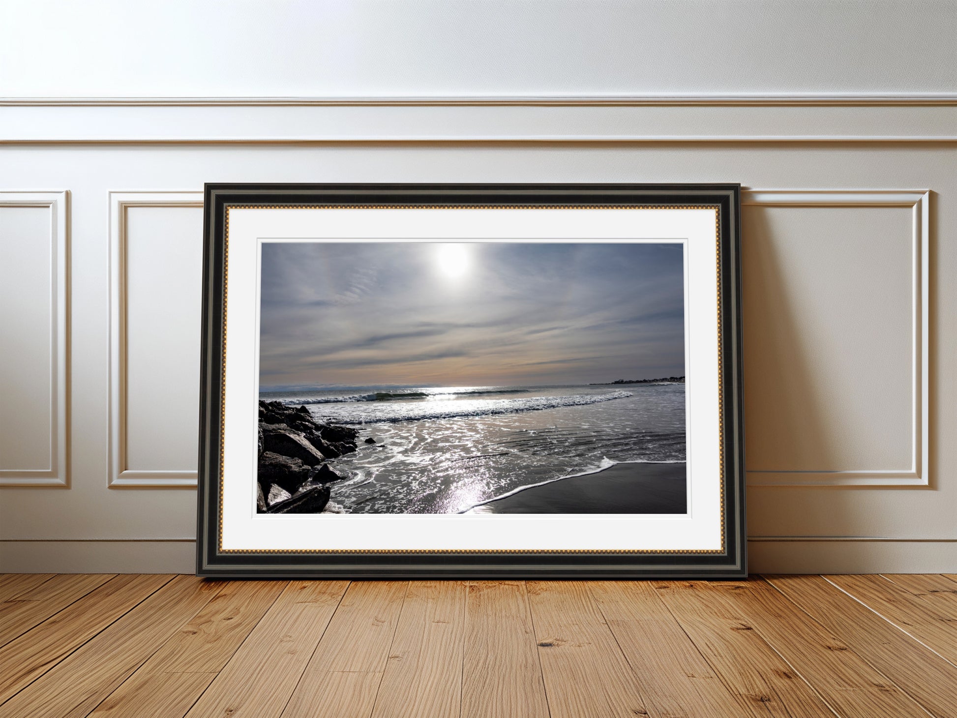 Framed photograph of a beach scene on a wooden floor with white walls.