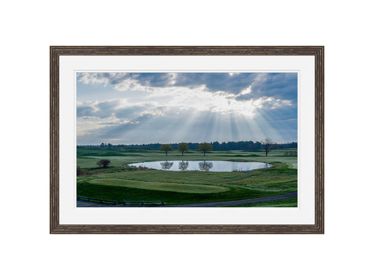Framed picture of a landscape with a lake and trees under a cloudy sky.